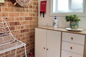 Una cocina con una silla de metal blanca, un armario con cajones, una planta en maceta y un extintor en la encimera.