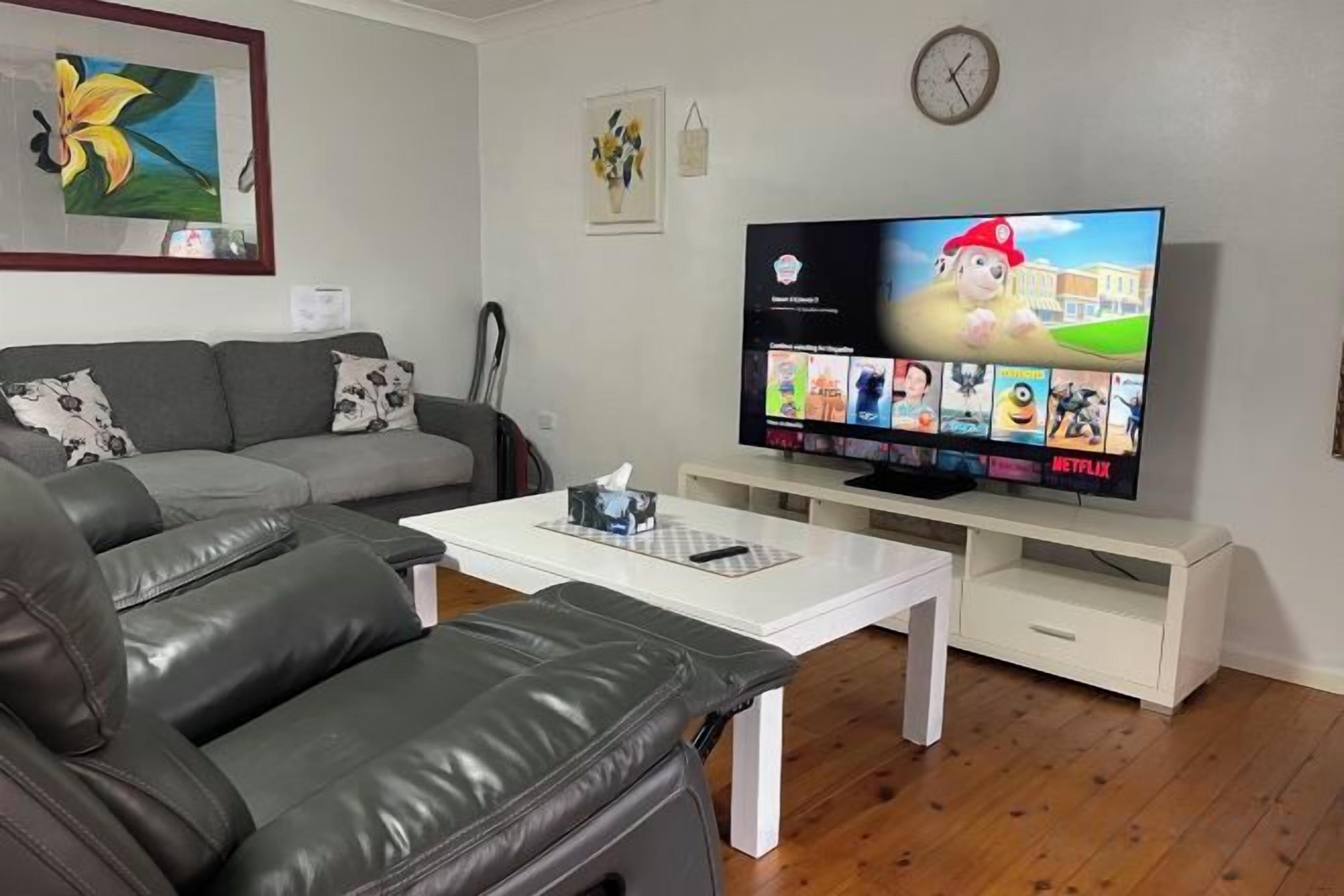 Una sala de estar con sofá, mesa de centro, televisor y un reloj en la pared.