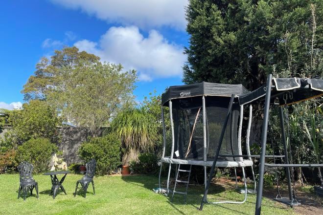 Un trampolín con red de seguridad, rodeado de césped y árboles.