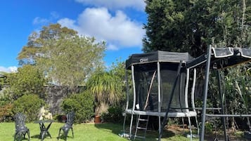 Un trampolín con red de seguridad, rodeado de césped y árboles.