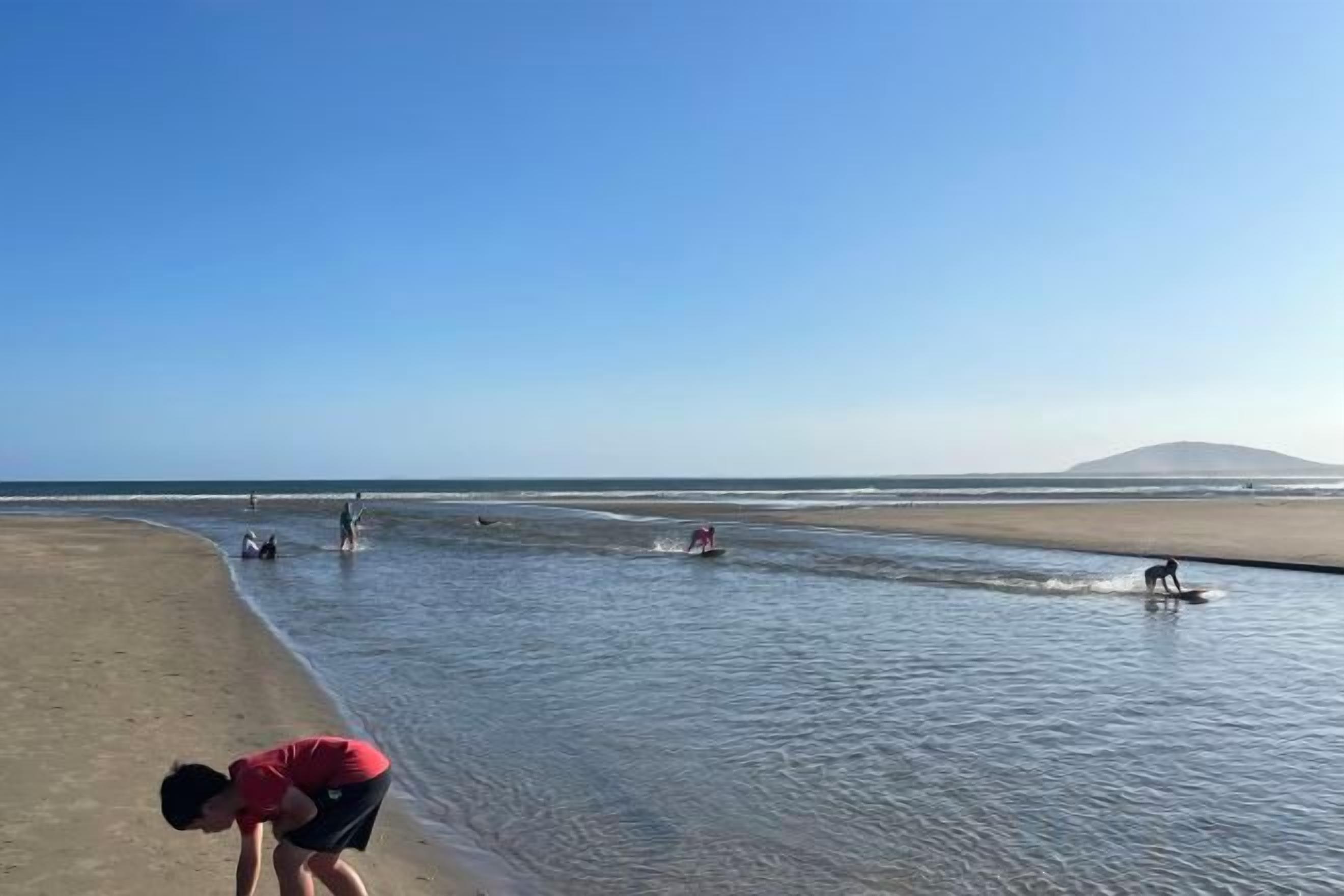 A beach with a clear sky, calm water, and a distant mountain.