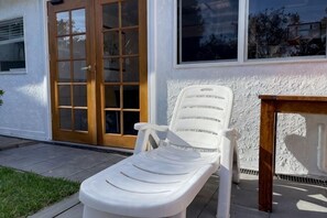 Una silla de jardín blanca de plástico frente a una casa con puerta y ventanas de madera.