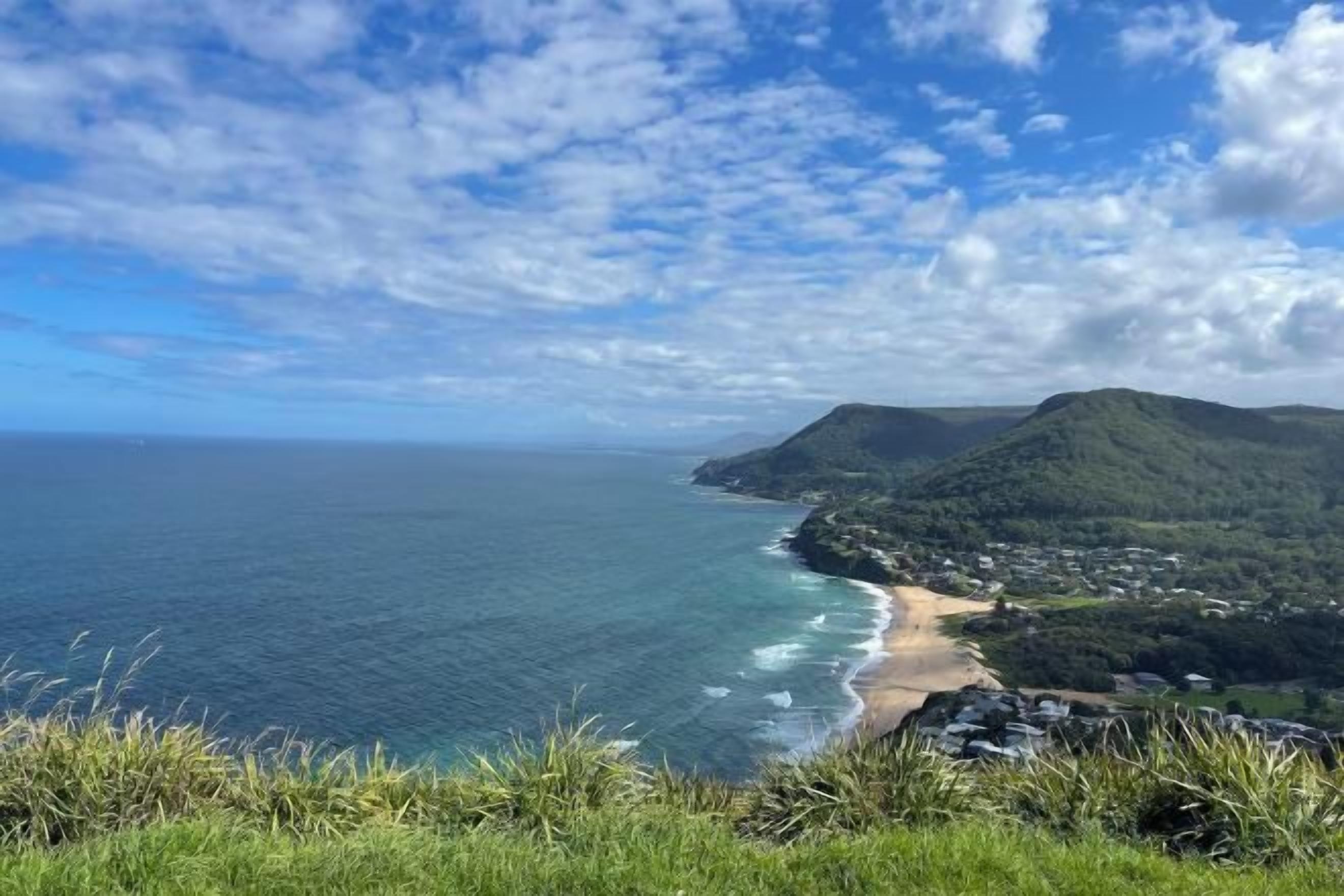 A coastal landscape with a beach, a mountain, and a clear sky.
