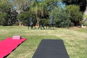 A backyard with a black mat, a red cloth, and two chairs around a table.