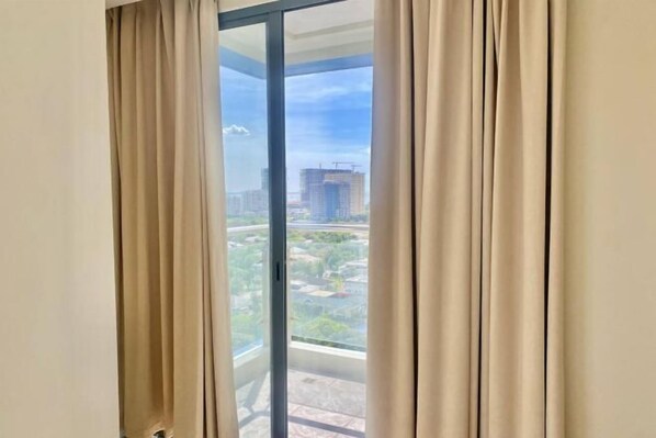 A room with a large window, curtains, and a view of a building and greenery outside. - City Center Business Hotel(Manila Airport and PITX) (Paranaque)