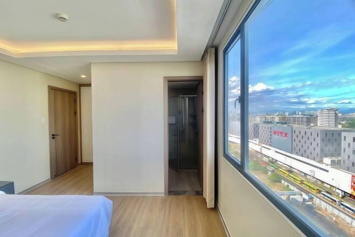 Una habitación de hotel moderna con un ventanal grande, una cama, una puerta y vistas de la ciudad.
