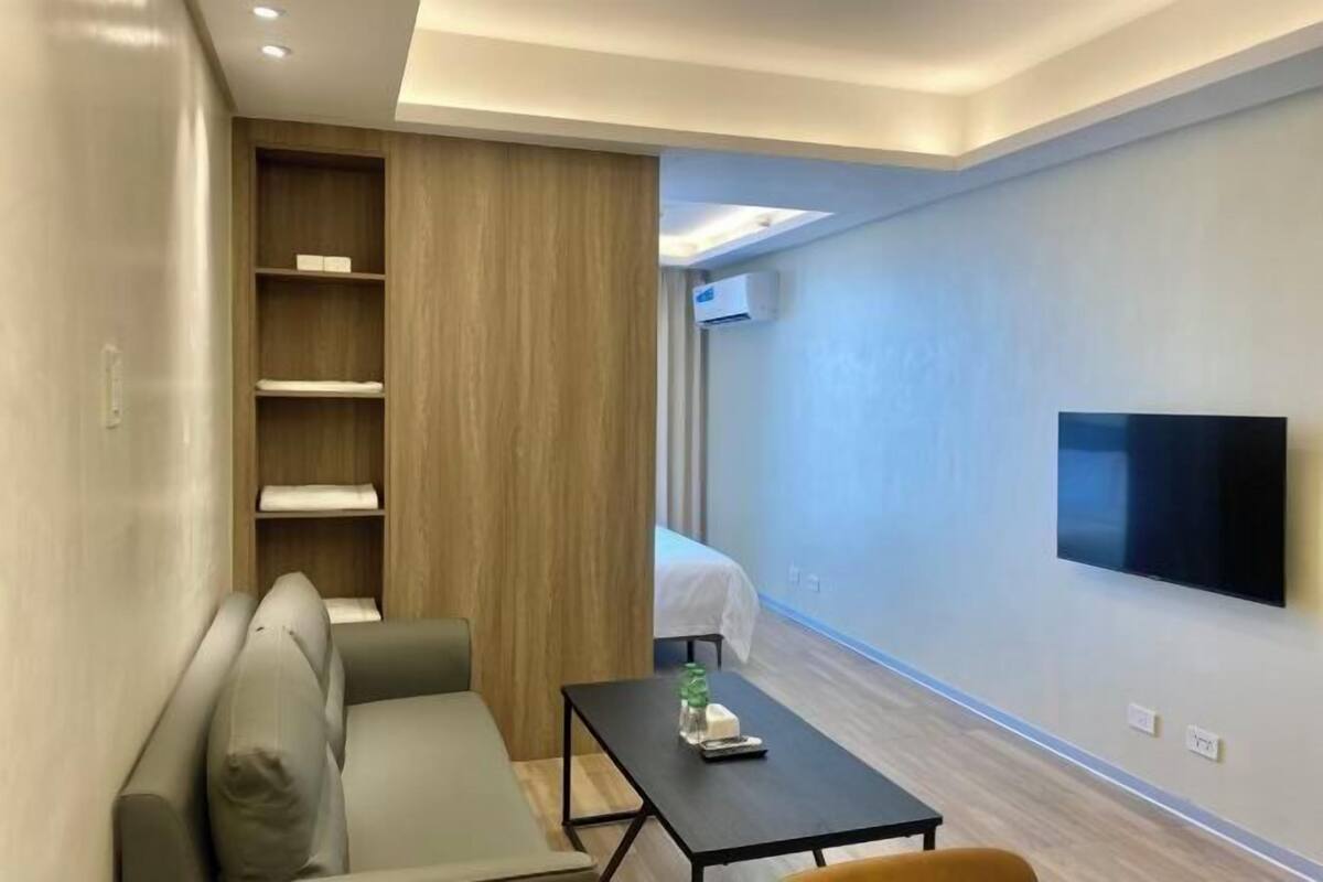 Una habitación de hotel moderna con sofá, una mesita, un televisor montado en la pared y un mueble de madera.