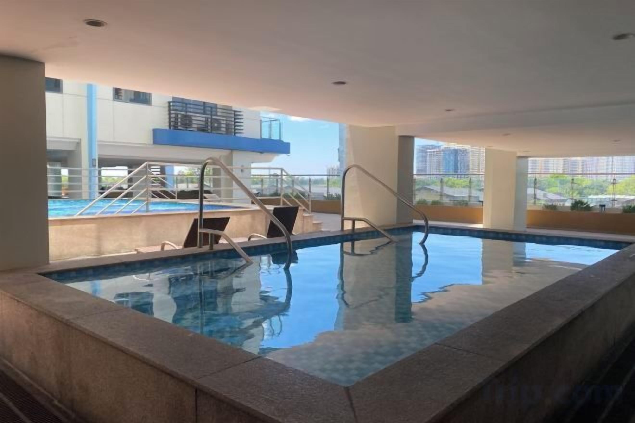 An indoor swimming pool with clear water, steps leading into the pool, and a view of buildings outside.