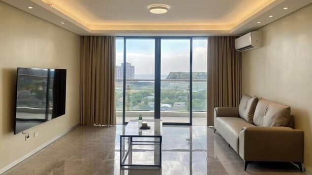 A modern living room with a flat-screen TV, a sofa, a coffee table, and a large window with a city view.
