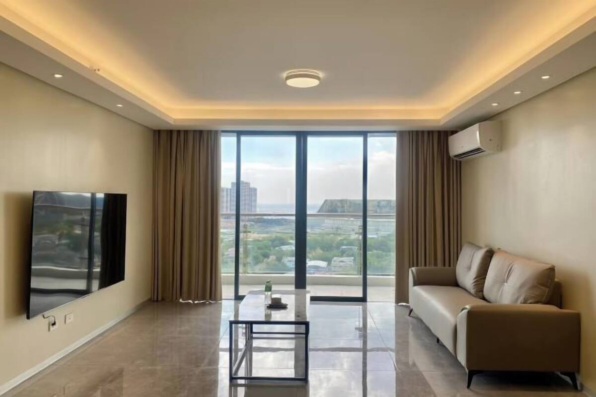 Una sala de estar moderna con un televisor de pantalla plana, un sofá, una mesa de centro y un ventanal con vistas a la ciudad.