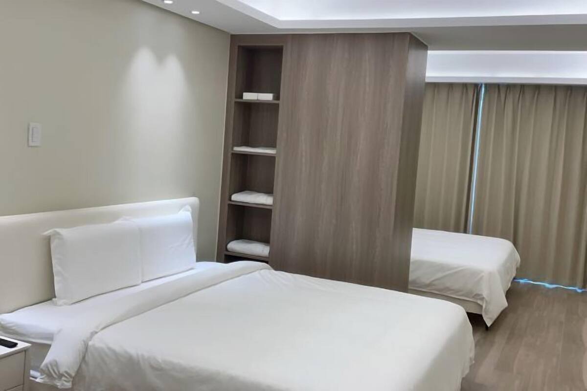 Habitación de hotel con una cama grande, una cama más pequeña, una mesita de noche, un armario y un ventanal con cortinas.