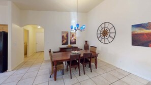 Een eetruimte met een houten tafel en stoelen, een kroonluchter, een wandklok en kunstwerken.