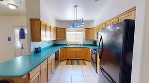 A kitchen with wooden cabinets, a black refrigerator, a blue countertop, and a window with a view. - Leisure Space - 327 (Moab)