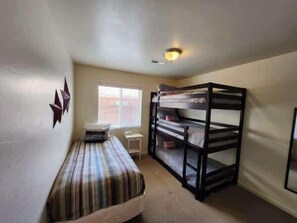 Habitación compacta con literas, una cama individual, un escritorio pequeño y una ventana.