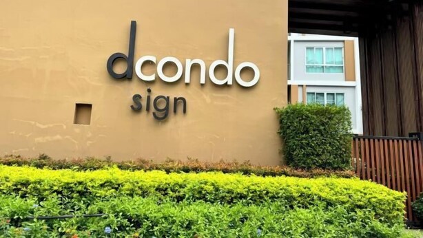 Een bord met de tekst 'dcondo sign', met een modern gebouw op de achtergrond.