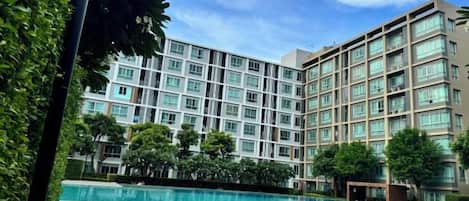 A hotel with a swimming pool, multiple floors, and a clear sky.