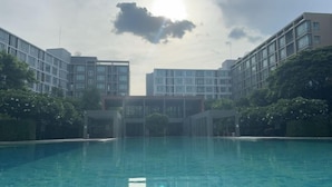 Een zwembad omringd door moderne gebouwen, met een heldere lucht en zonlicht.