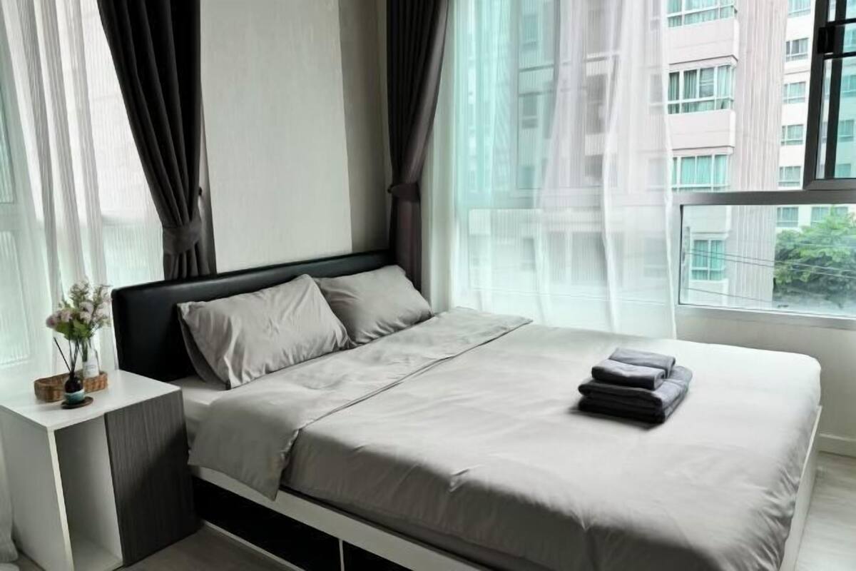 Ein modernes Schlafzimmer mit einem Bett, Vorhängen und Blick auf Gebäude durch das Fenster.