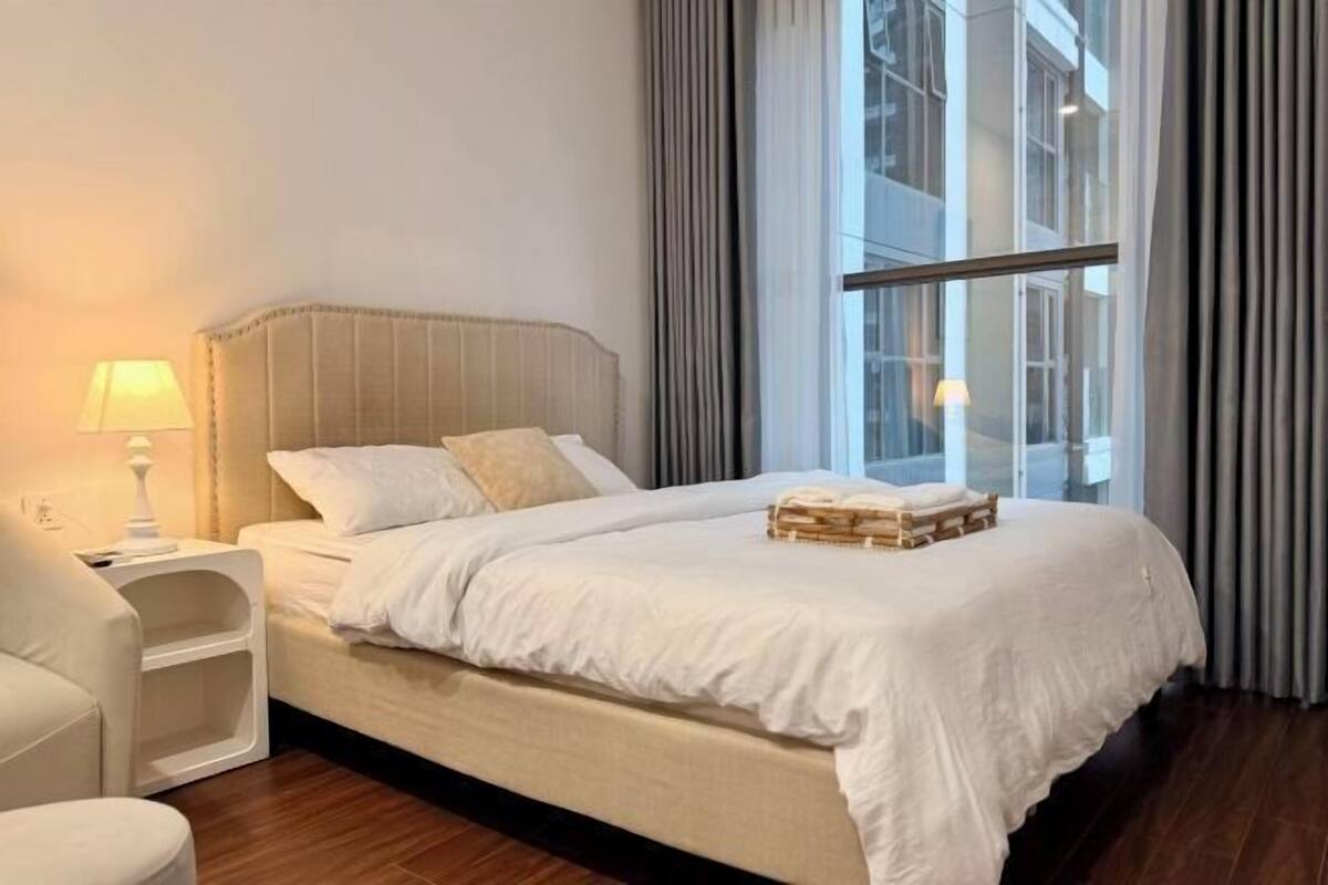 Une chambre d’hôtel équipée d’un lit, d’une table de chevet, d’une lampe et offrant une vue sur la ville grâce à de grandes fenêtres.