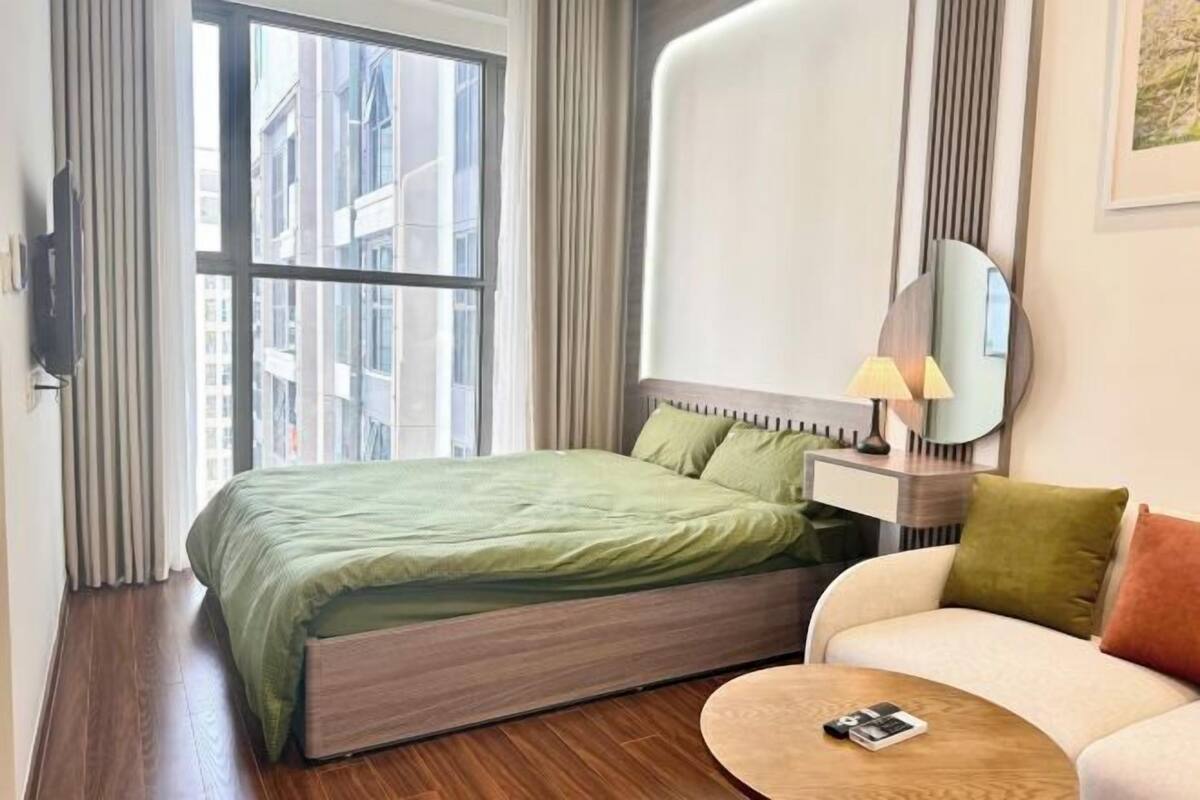 Une chambre d’hôtel avec un lit, un canapé, une petite table, un miroir et une fenêtre avec des rideaux.