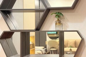 A modern interior with a geometric wall design, a plant on a shelf, and a glimpse of a bed and seating area in the background. - A Quiet Stay - Service Apartment, Vinhome Ocean Park, Ha Noi (Hanoi)