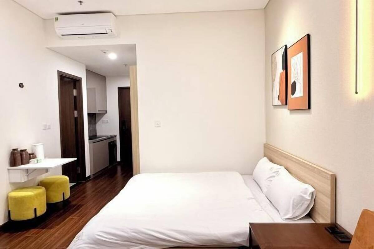 Une chambre d’hôtel comprenant un lit, un bureau, une chaise, une petite table, un climatiseur fixé au mur et une porte donnant sur une kitchenette.