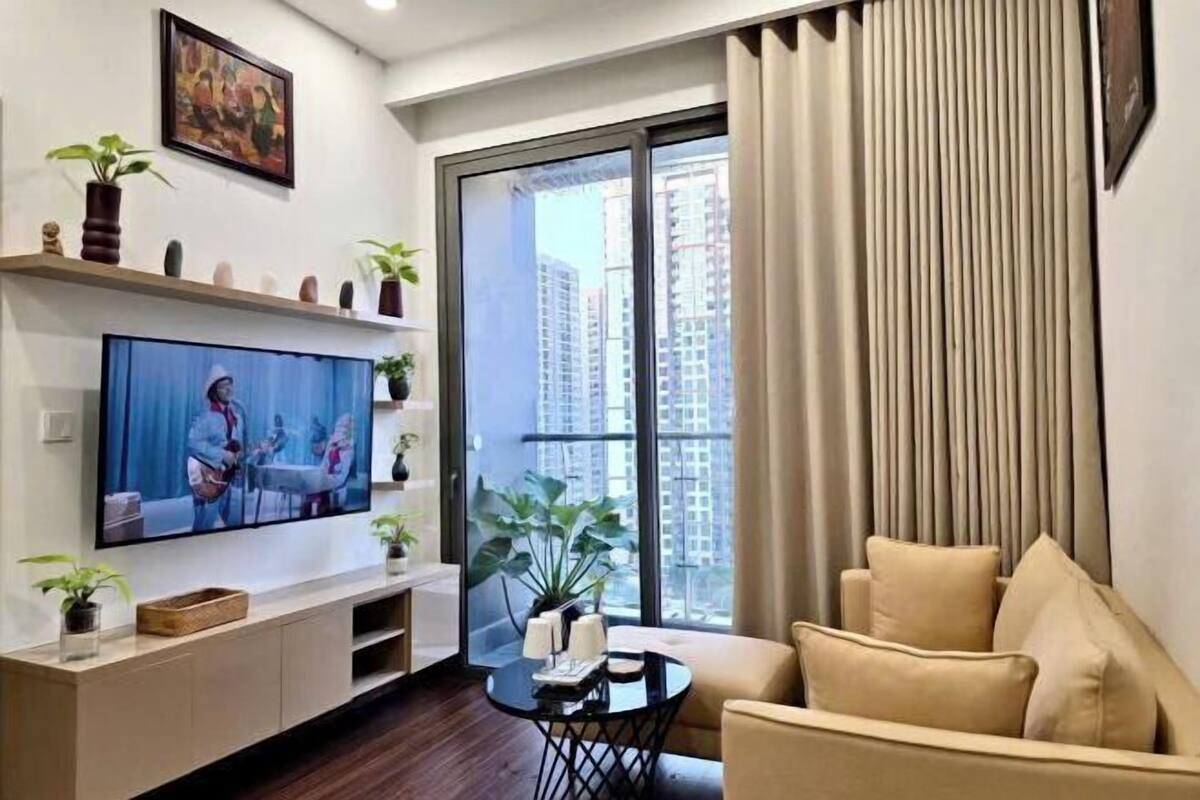 Un salon moderne doté d’un téléviseur à écran plat, d’un canapé, d’une petite table basse et d’un balcon offrant une vue sur les immeubles de grande hauteur.