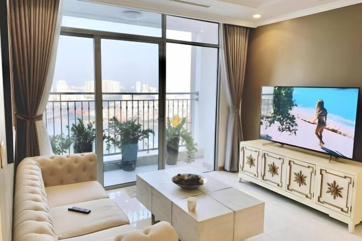 Una sala de estar con sofá, mesa de centro, televisor y balcón con plantas.