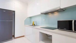 A modern kitchen with white cabinetry, a stainless steel refrigerator, a black microwave, and a sink with a faucet. - The Landmark Platinum - Vinhomes Central Park (Ho Chi Minh City)