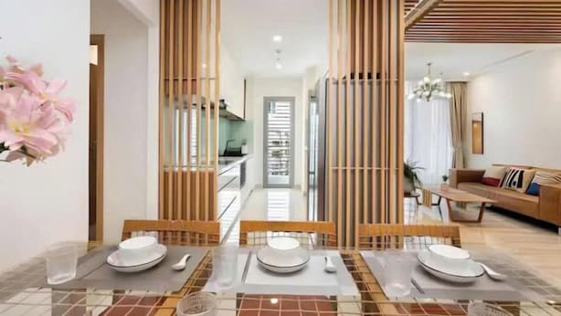A dining area with a table set for four, a kitchen in the background, and a living area with a sofa and a chandelier. - The Landmark Platinum - Vinhomes Central Park (Ho Chi Minh City)