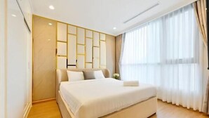 A modern hotel room with a large bed, a wooden floor, a wall-mounted light panel, and a large window with curtains. - The Landmark Platinum - Vinhomes Central Park (Ho Chi Minh City)