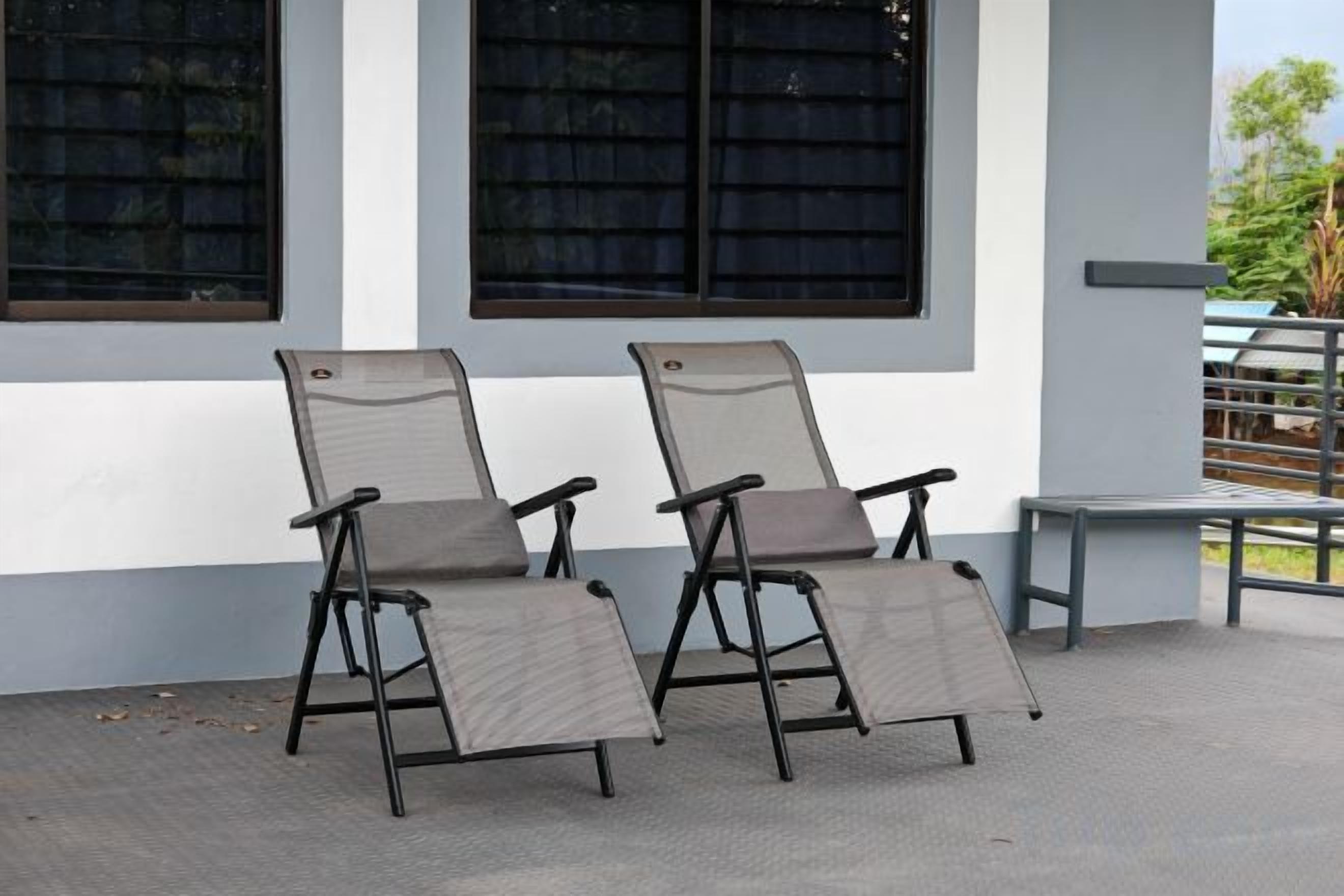 Two outdoor chairs with a metal frame and fabric seat, positioned on a concrete surface in front of a building with large windows.