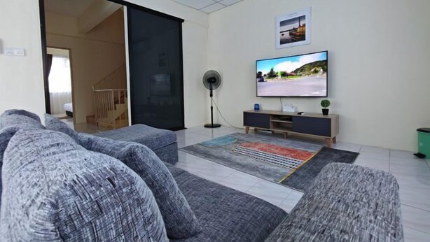 A modern living room with grey sofas, a flat-screen TV, a floor fan, and a colorful rug. - Riverside Lot No.1 Homestay at Kota Kinabalu (Putatan)