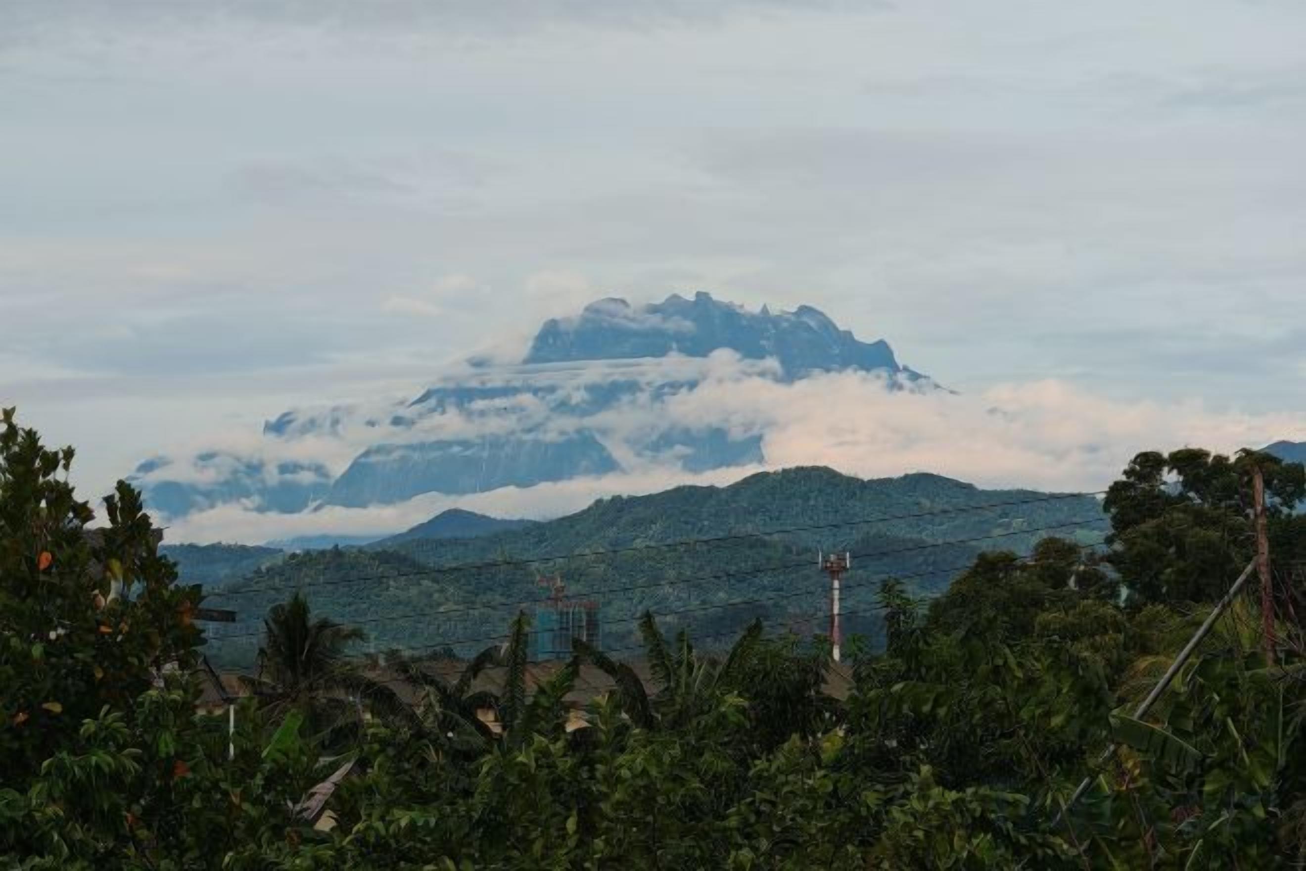 A mountain range with clouds in the background and vegetation in the foreground.