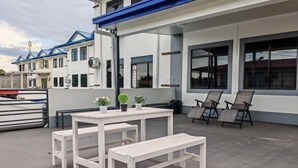A white outdoor seating area with a table and benches, potted plants, and a view of a building with blue roofs. - Riverside Lot No.1 Homestay at Kota Kinabalu (Putatan)