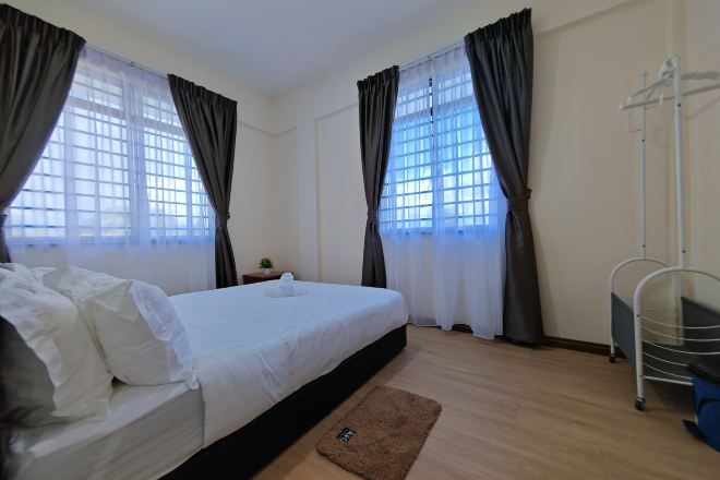 Un dormitorio con cama, cortinas, una ventana, una mesita de noche y un pequeño tapete.