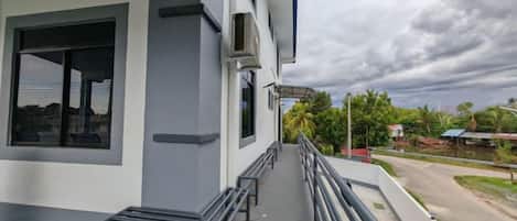 A building with a balcony, a bench, and a view of a road and greenery.