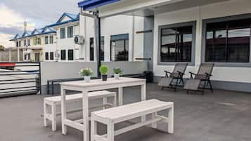 Un espace extérieur aménagé avec une table et des bancs, une poubelle et un bâtiment doté de grandes fenêtres et d’un toit bleu.
