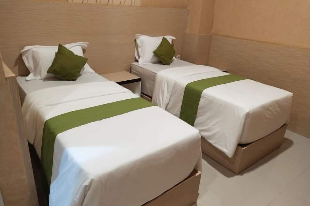 A room with two beds, each with a pillow and a green bedspread.