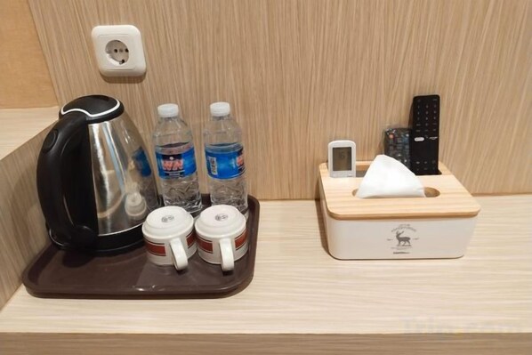 A tray with a kettle, water bottles, and mugs on a wooden surface. - HOTEL KEMBANG JOYO (South Palu)
