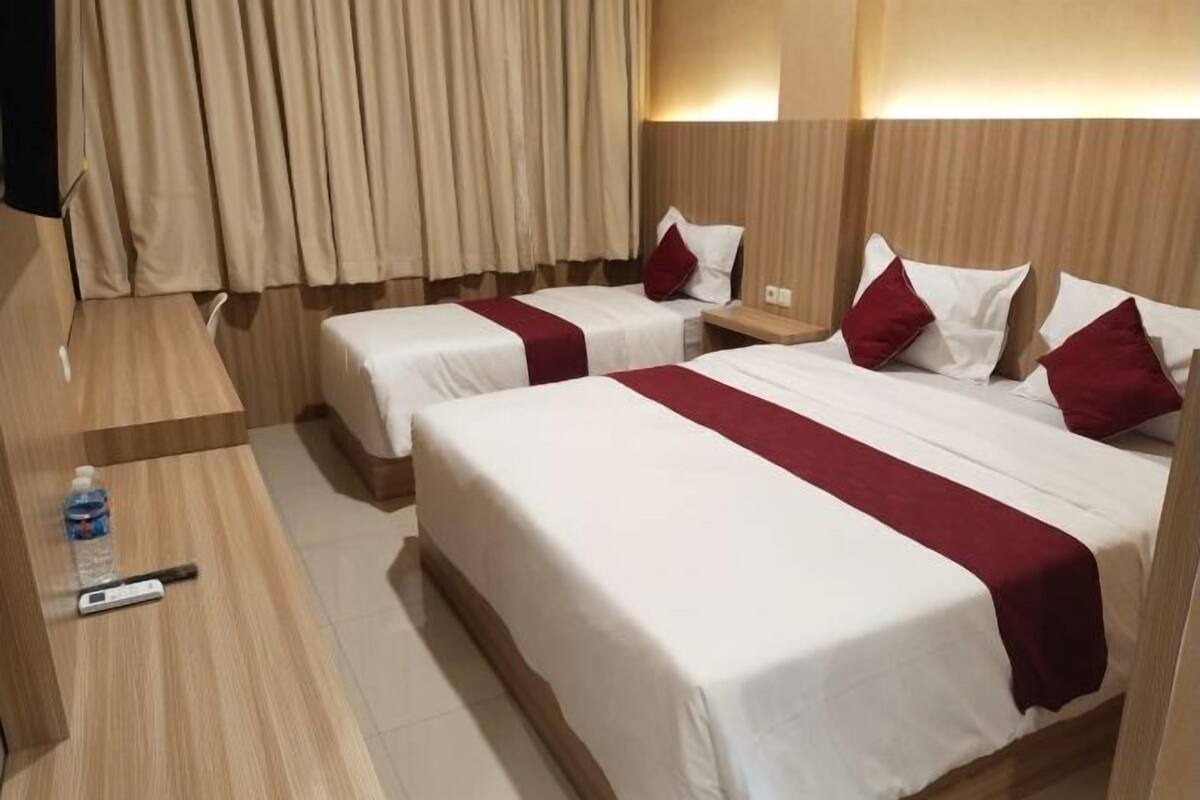 A hotel room with two beds, a wooden desk, a remote control, and a water bottle.