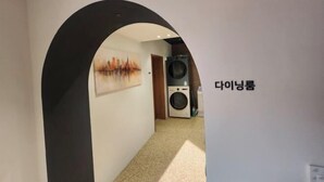 Un couloir avec une grande arche noire menant à une buanderie équipée d’un lave-linge et d’un sèche-linge.