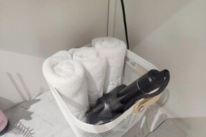 A white basket containing rolled towels and a black object, possibly a hairdryer, on a white surface. - Stay plan (Incheon)