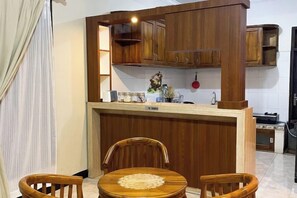 Μια μικρή, λειτουργική κουζίνα με ξύλινα ντουλάπια, ένα μικρό πάγκο-νησίδα και μια τραπεζαρία με δύο καρέκλες.