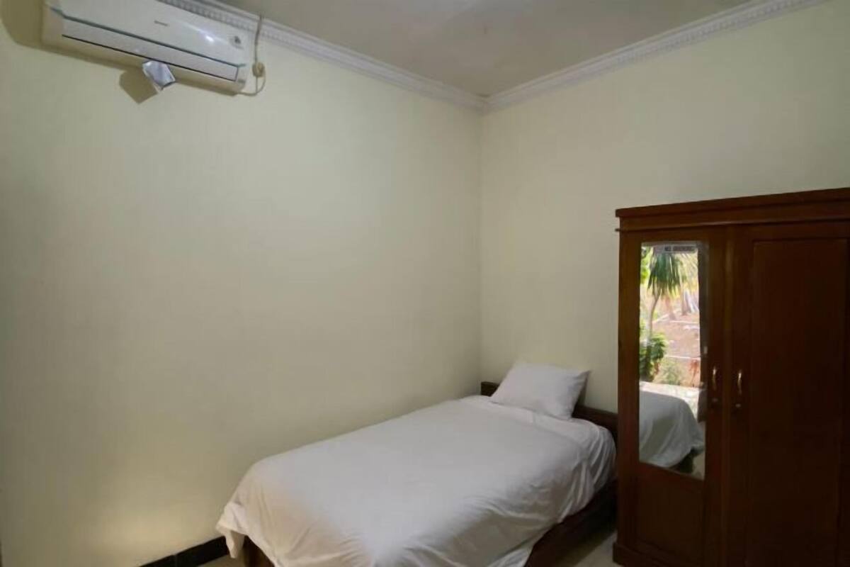 A small, single-bed room with a wooden wardrobe and an air conditioning unit on the wall.
