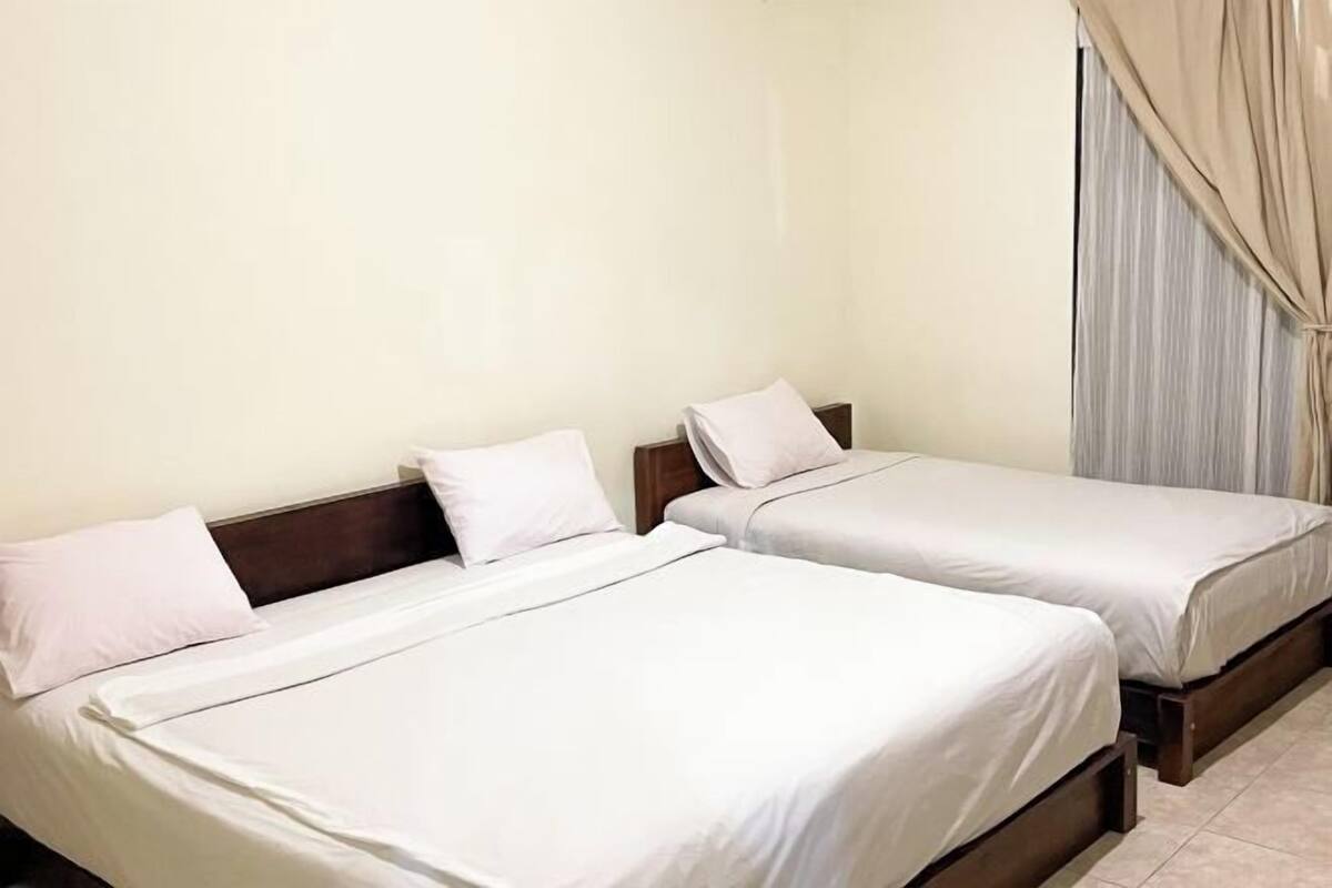 A hotel room with two single beds, a wooden headboard, and a window with curtains.