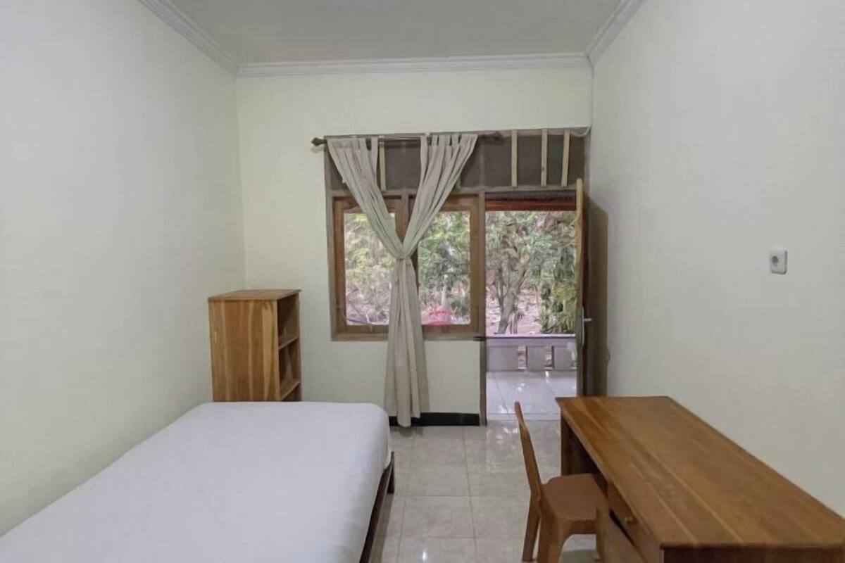 A room with a bed, a wooden desk, a chair, a wooden wardrobe, and a window with curtains.