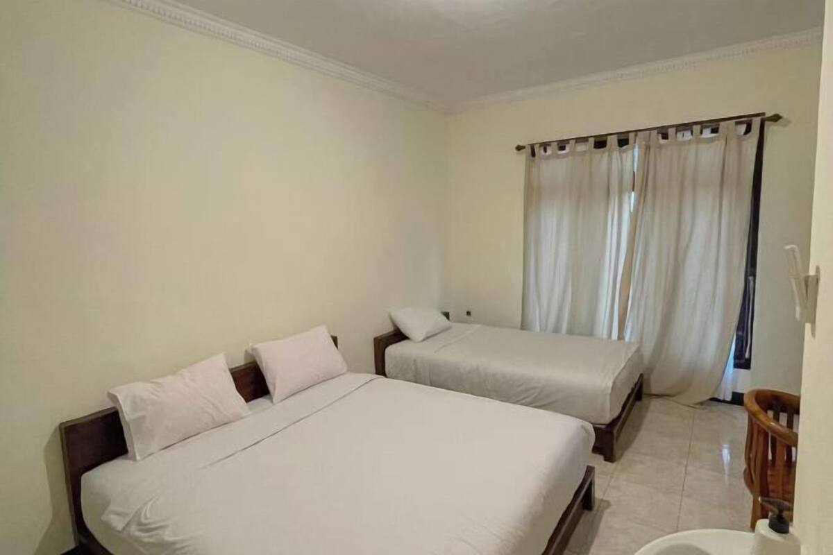 A room with two beds, a wooden chair, a curtain, and a tiled floor.