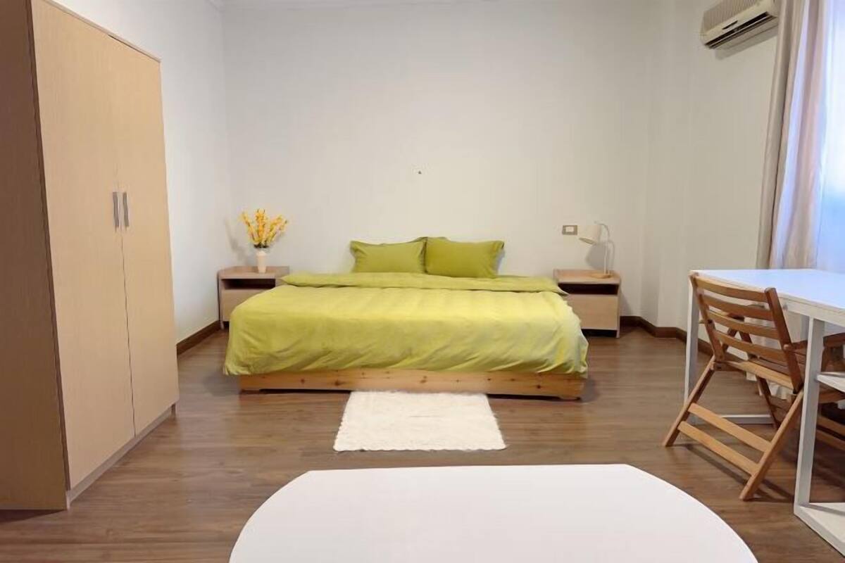A bedroom with a bed, bedside tables, a desk, and a wardrobe.