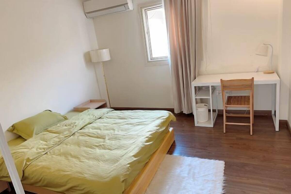 A bedroom with a bed, a desk, a chair, a lamp, and a window.